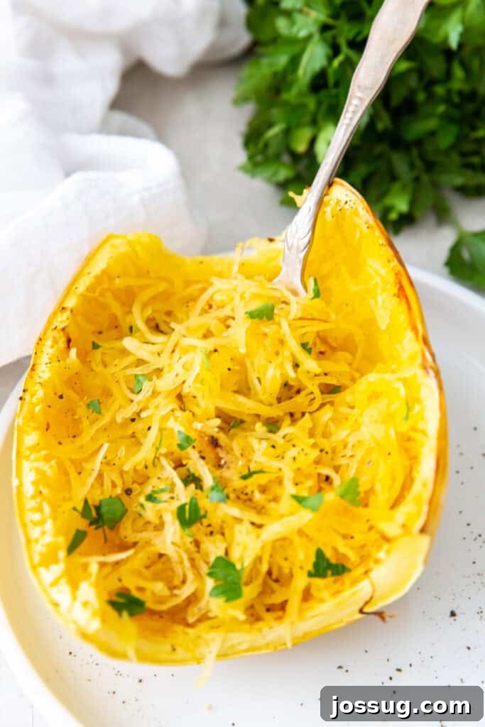 Effortless Air Fryer Spaghetti Squash 59 Roasted spaghetti squash half on a plate with a fork, strands fluffed and garnished with parsley.