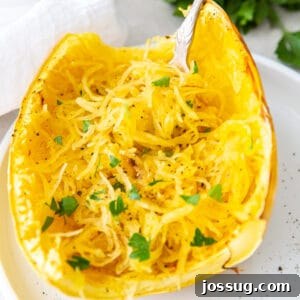 Close-up of roasted spaghetti squash half with fork and parsley garnish, square crop for social sharing.
