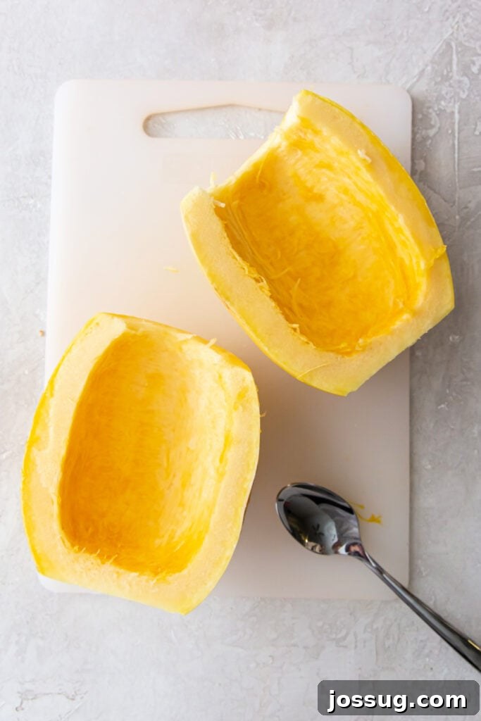 Two spaghetti squash halves with seeds removed, cleaned out and ready for cooking, on a cutting board with a spoon.