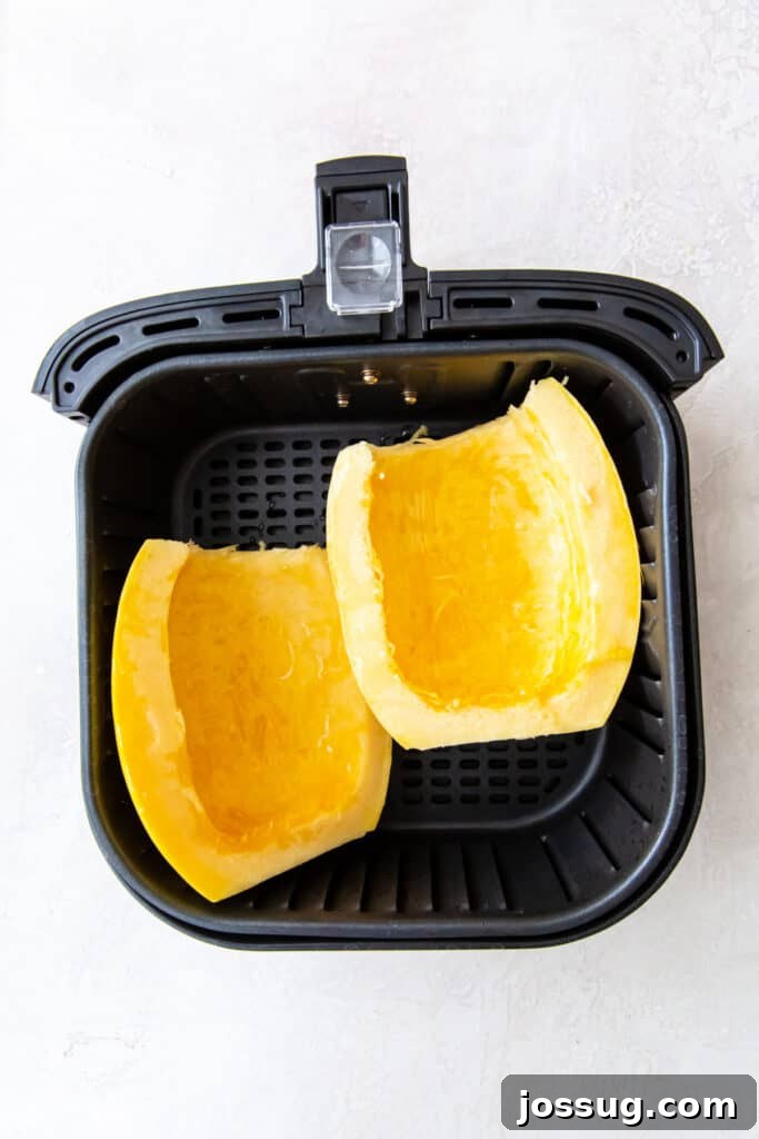 Two cleaned spaghetti squash halves placed cut side up in an air fryer basket.