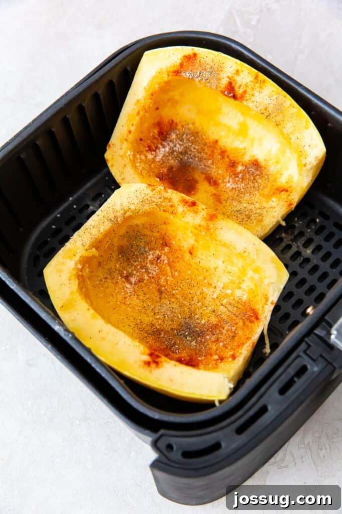 Spaghetti squash halves in an air fryer basket seasoned with paprika, salt, and pepper.