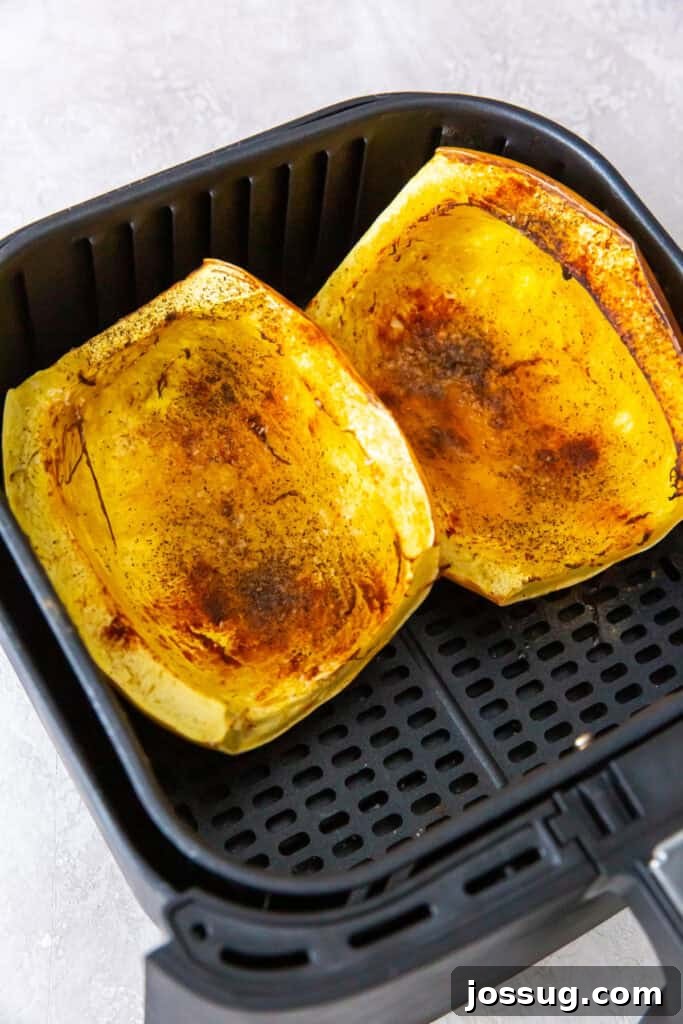 Roasted spaghetti squash halves in an air fryer basket with browned and seasoned edges.