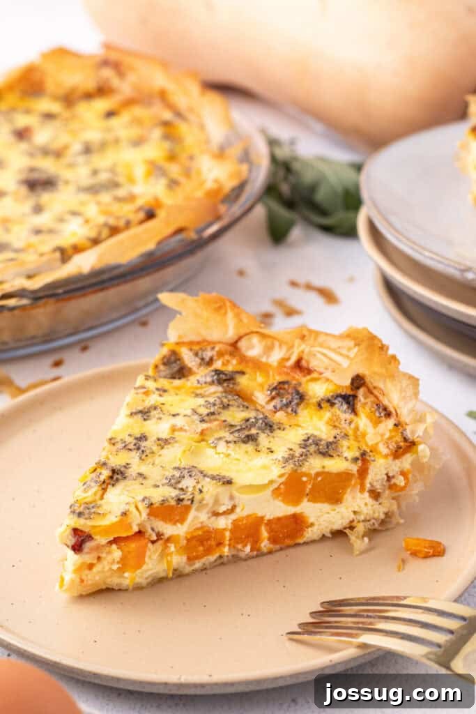 Slice of roasted squash quiche on a beige plate with a golden phyllo crust, fork nearby, and the rest of the quiche in the background.