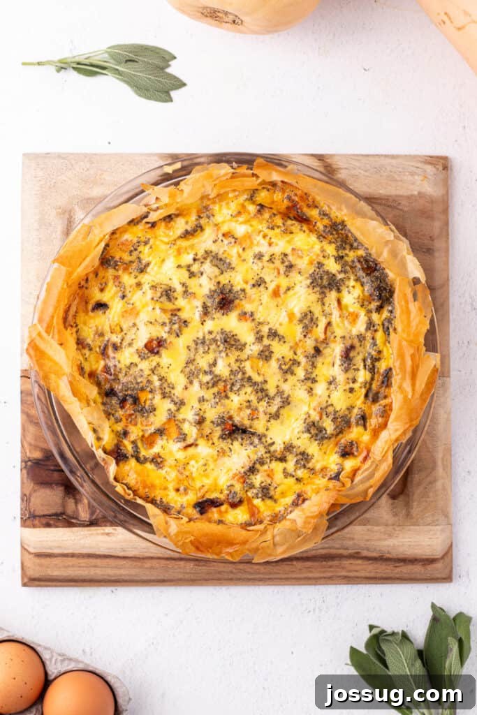 Baked roasted squash quiche in a phyllo crust, golden brown on top and resting on a wooden board with fresh sage nearby.