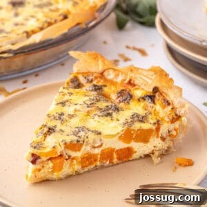 Square cropped photo of roasted squash quiche slice on a beige plate, with golden phyllo edges and visible chunks of butternut squash.
