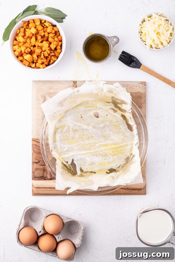 Close up of phyllo dough brushed with olive oil in a pie dish, with ingredients like squash, cheese, eggs, milk, and sage nearby.