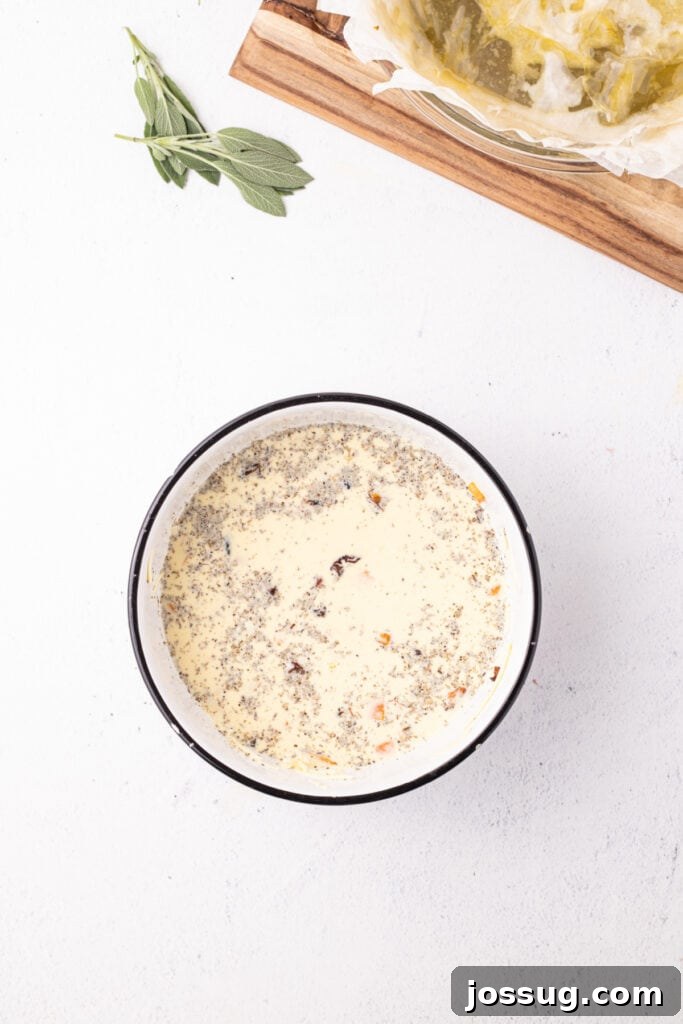 Bowl with quiche filling mixture of eggs, cream, squash, cheese, and sage, seasoned and ready to pour into the crust.