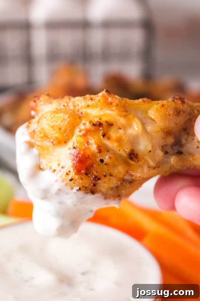 Hand dipping a crispy lemon pepper chicken wing into creamy ranch dressing with fresh celery and carrots in the background, ready for serving.