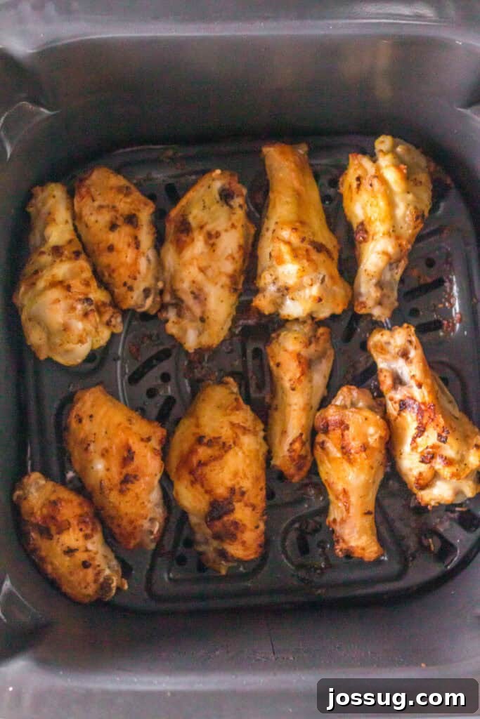 Golden brown lemon pepper chicken wings cooking in an air fryer basket.