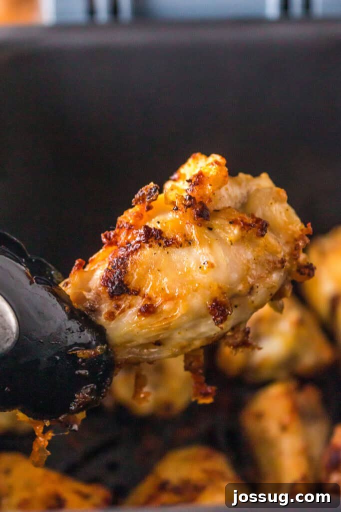 Close-up of a perfectly crispy air fryer lemon pepper chicken wing held with tongs over the basket, showcasing its golden exterior.
