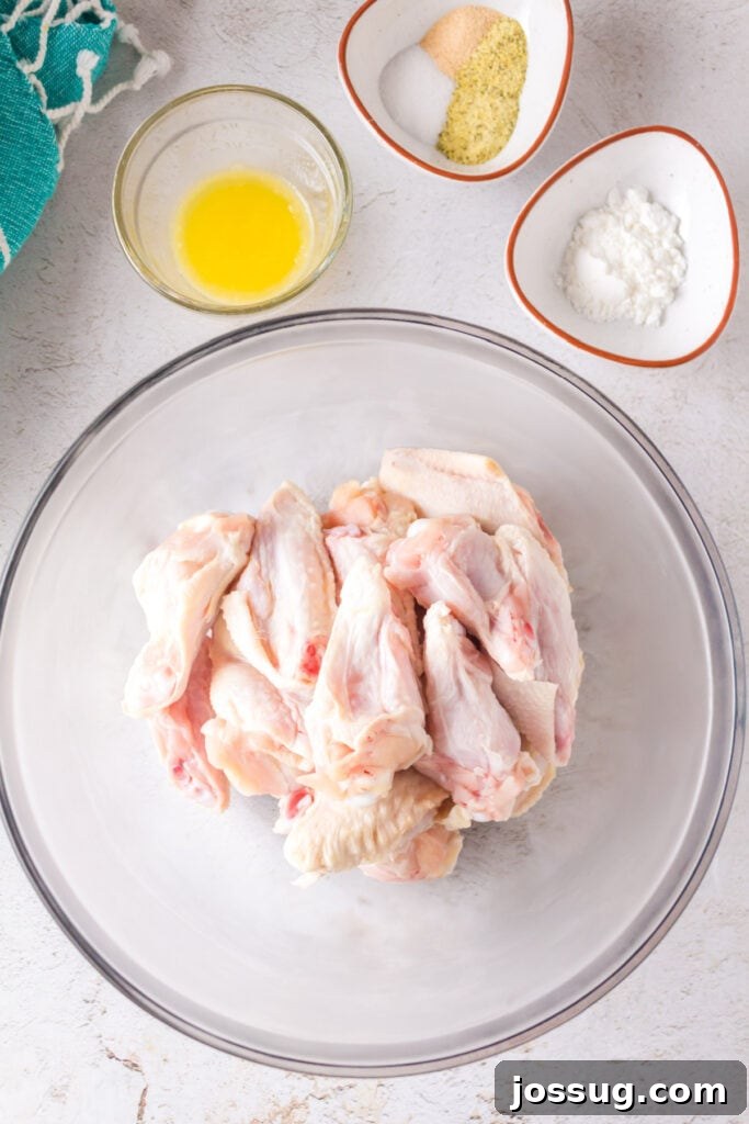 Crispy Air Fryer Lemon Pepper Wings 4 Raw chicken wings in a glass bowl with melted butter, seasoning mix, and cornstarch in small bowls nearby.