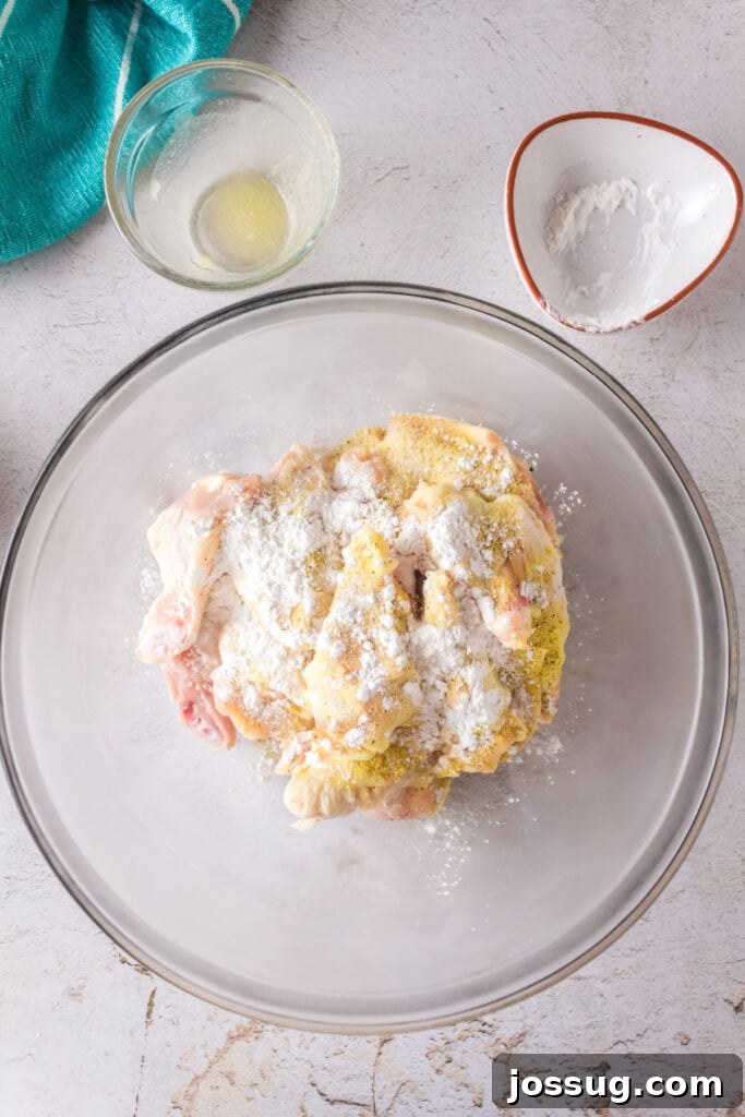 Chicken wings coated with seasoning and lightly dusted with cornstarch in a mixing bowl.