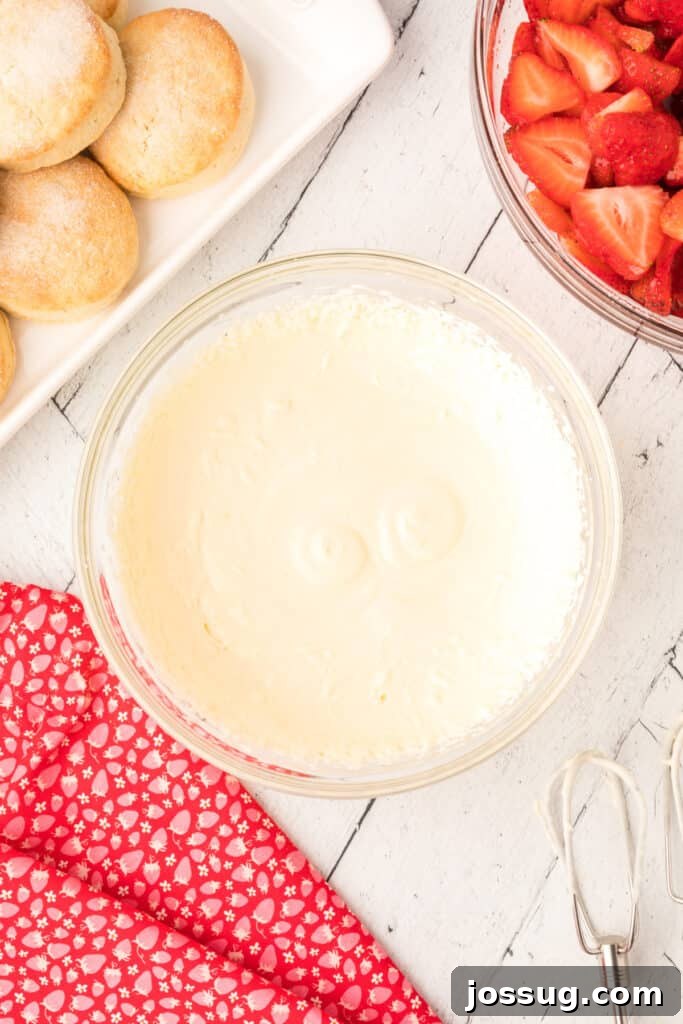 Light and airy whipped lemon cream in a glass bowl, showcasing its fluffy texture, with fresh strawberries and baked shortcakes nearby, ready for assembly.