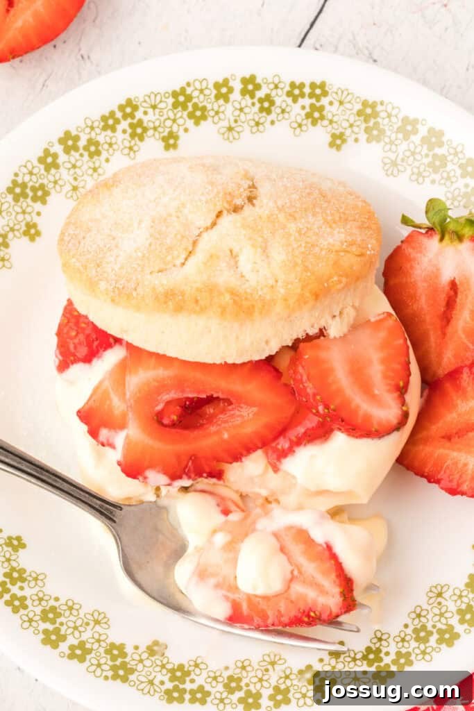 A close-up of a partially eaten Strawberry Shortcake with Lemon Cream Sauce, showing the fluffy biscuit, generous strawberries, and creamy topping. A fork rests on the plate, inviting another bite.