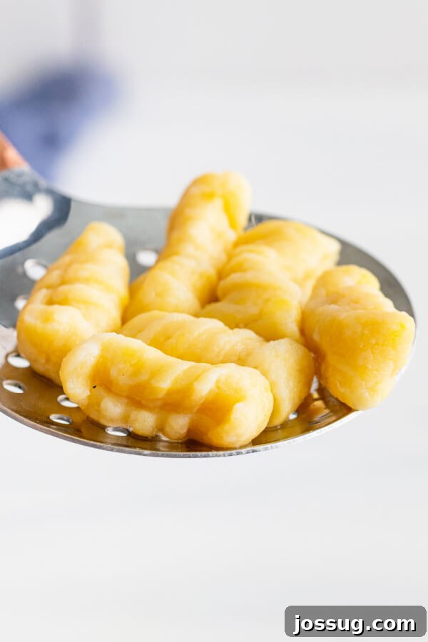 Pillowy Soft Potato Gnocchi 3 Close-up of freshly cooked potato gnocchi being lifted out of boiling water with a metal spider strainer