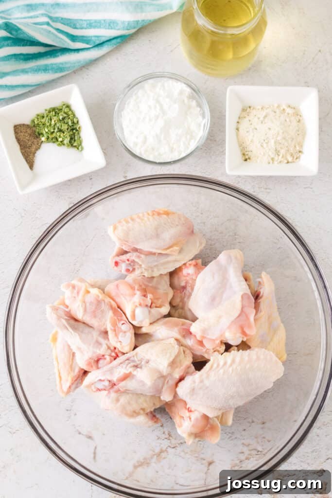 Crispy Air Fryer Ranch Wings 3 Raw chicken wings in a glass bowl surrounded by olive oil, cornstarch, seasoning mix, and spices on a white counter