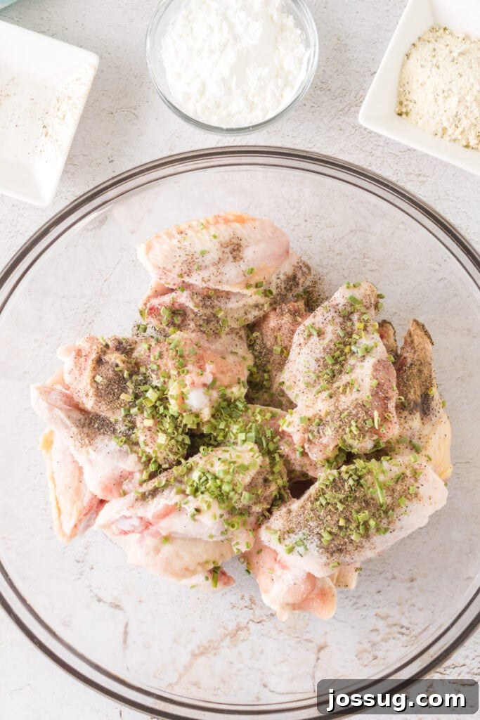 Crispy Air Fryer Ranch Wings 5 Chicken wings in a glass bowl sprinkled with salt, pepper, and chives before mixing