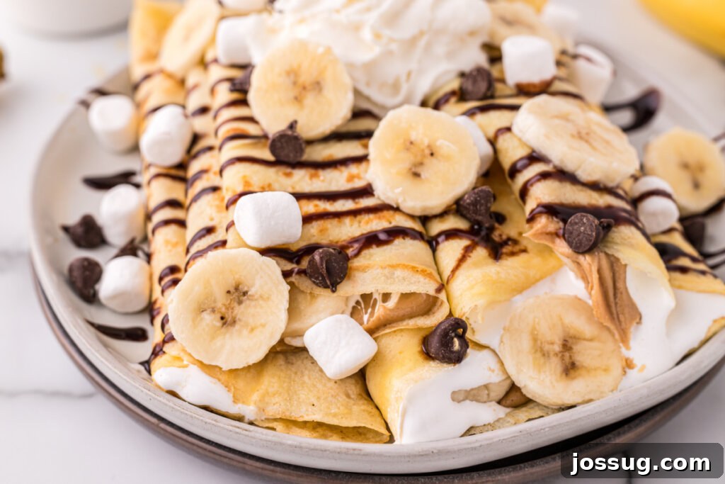 Decadent Banana Fluffernutter Crepes 5 Two perfectly rolled banana fluffernutter crepes, generously topped with chocolate sauce and whipped cream, resting on a rustic white plate.