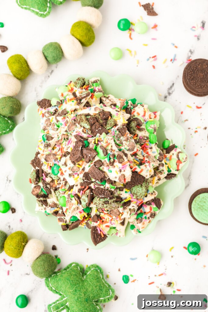 A top-down view of a mint green plate piled high with vibrant green Loaded Leprechaun Mint Bark, adorned with colorful M&M's, crushed Oreo cookies, and rainbow sprinkles.
