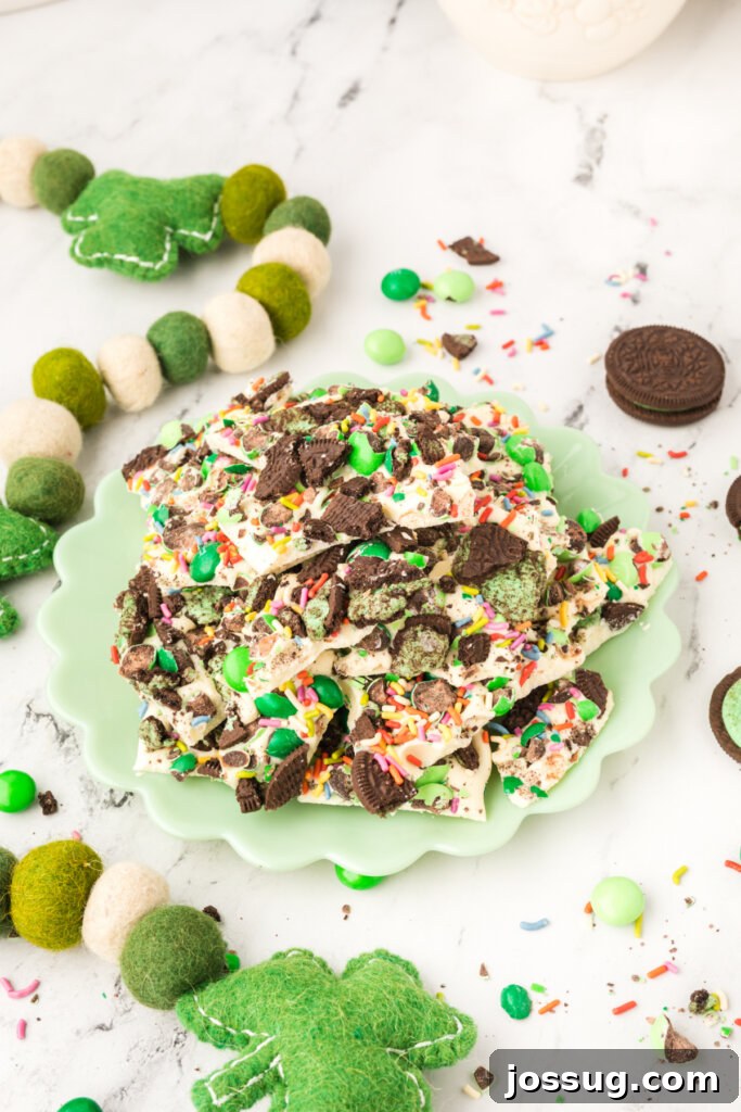 A vibrant display of numerous Loaded Leprechaun Mint Bark pieces, adorned with green candies and crushed cookies, arranged artistically on a mint green ceramic plate, ready to be sampled and enjoyed.