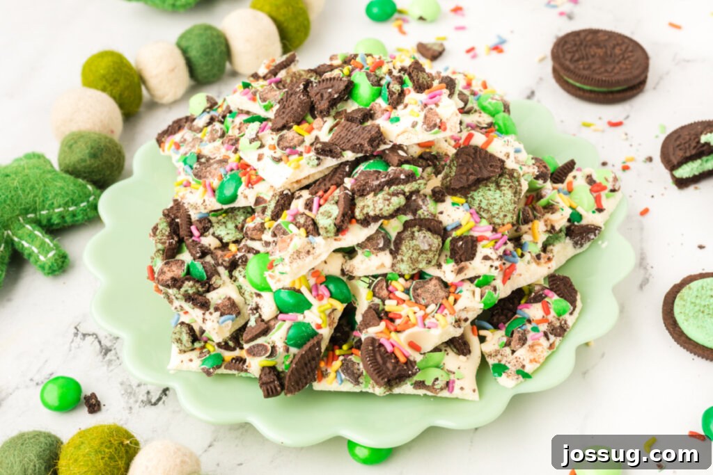 Close-up of several pieces of vibrant green mint bark, richly topped with M&M's, crushed Oreos, and sprinkles, presented on a bright green ceramic plate, ready to be served.
