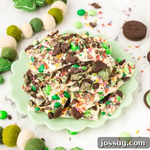 A top-down view of vibrant green mint bark pieces, generously topped with an assortment of M&M's, crushed Oreos, and colorful sprinkles, arranged on a bright green plate.