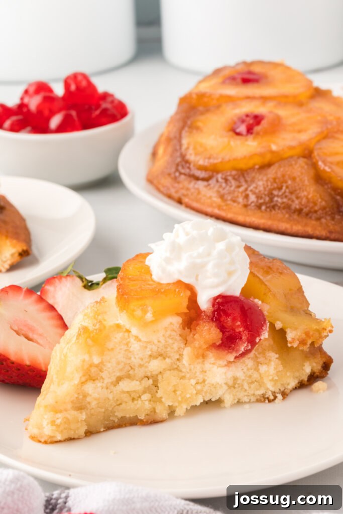 A perfectly portioned slice of pineapple upside-down cake with a maraschino cherry on top, sitting on a white plate