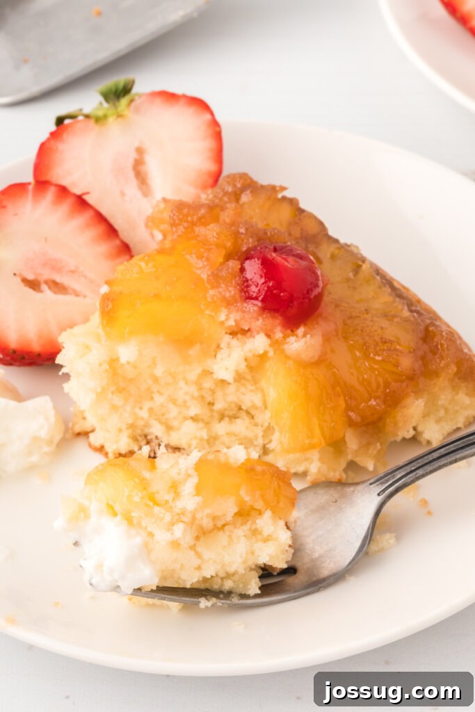 A fork holding a bite of pineapple upside-down cake, showing the moist cake and caramelized fruit