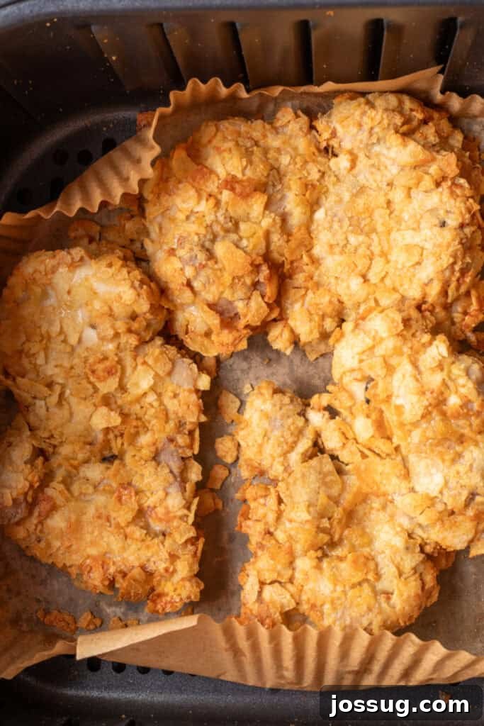 Four breaded chicken thighs with a crunchy potato chip coating neatly arranged inside an air fryer basket lined with parchment paper.