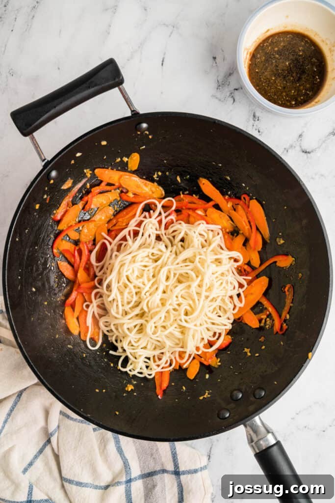 Cooked lo mein noodles added to the wok with the sautéed vegetables, ready for combining.
