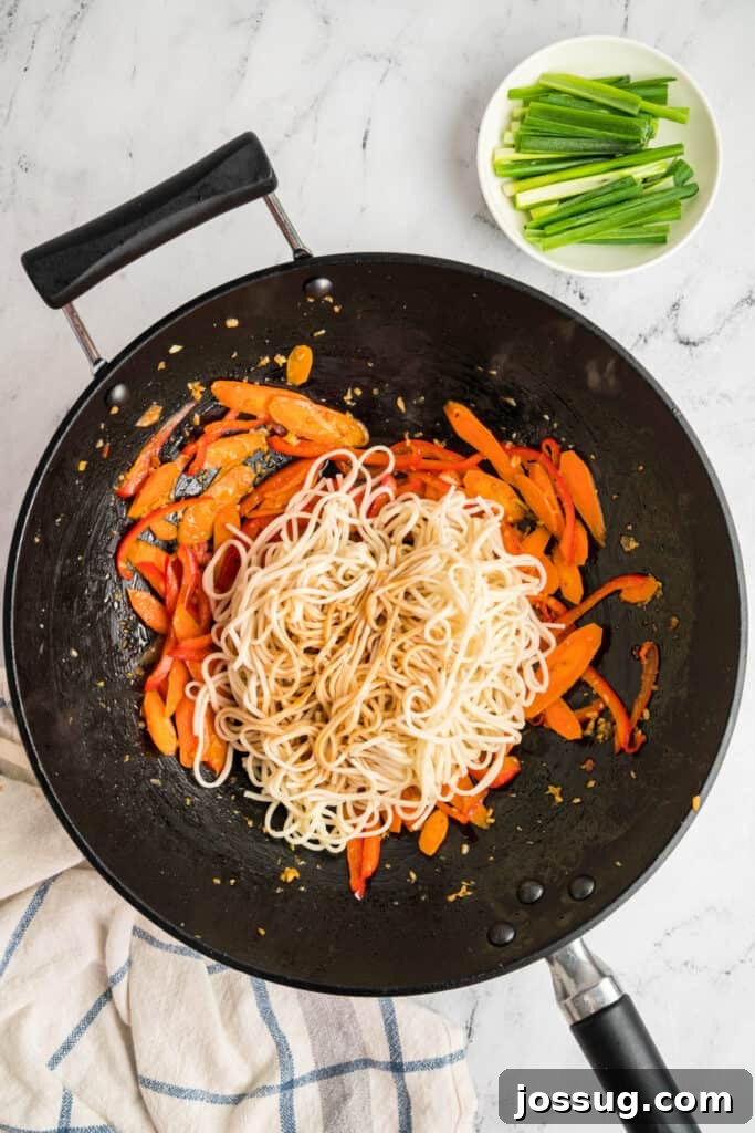 Lo mein sauce poured over the noodles and vegetables in the wok, ready to be mixed, ensuring full coating.