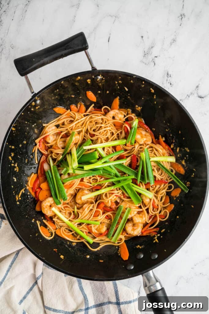 Green onions added on top of the shrimp lo mein in a wok before final mixing, adding fresh flavor.
