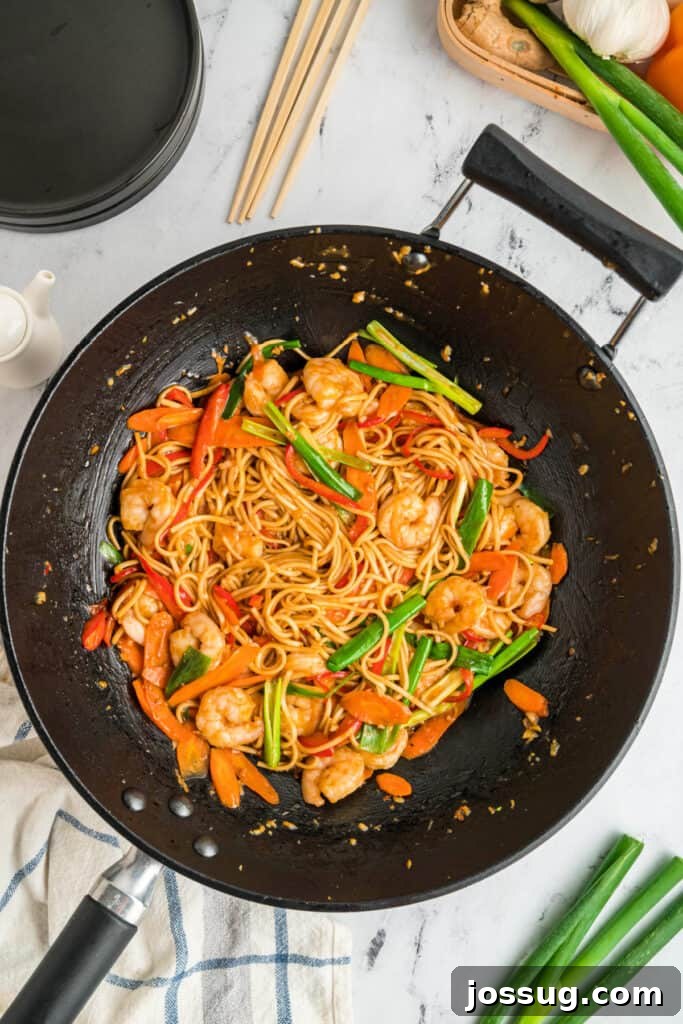 Finished shrimp lo mein in a wok with shrimp, vegetables, and noodles coated in sauce, steaming hot and ready.