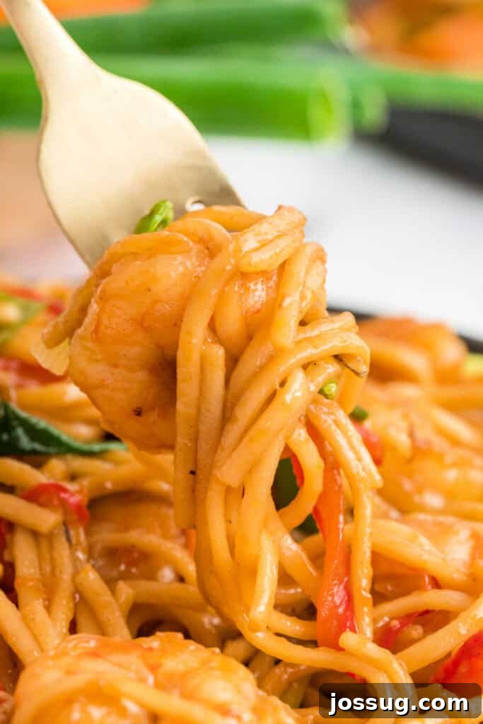 Close-up of a fork twirling noodles and shrimp coated in sauce, invitingly presented.