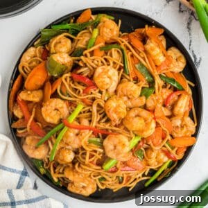 Square overhead image of shrimp lo mein with shrimp, noodles, and vegetables served on a black plate.