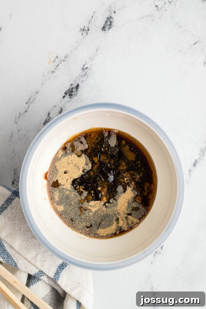 Lo mein sauce in a bowl with white pepper and other spices sprinkled on top before mixing, ready for whisking.