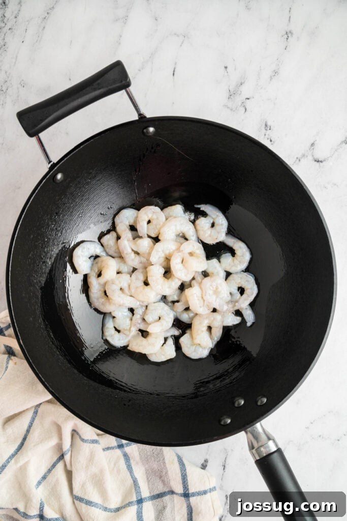 Raw shrimp in a black wok with oil, beginning to cook for shrimp lo mein, illustrating the first step of cooking.