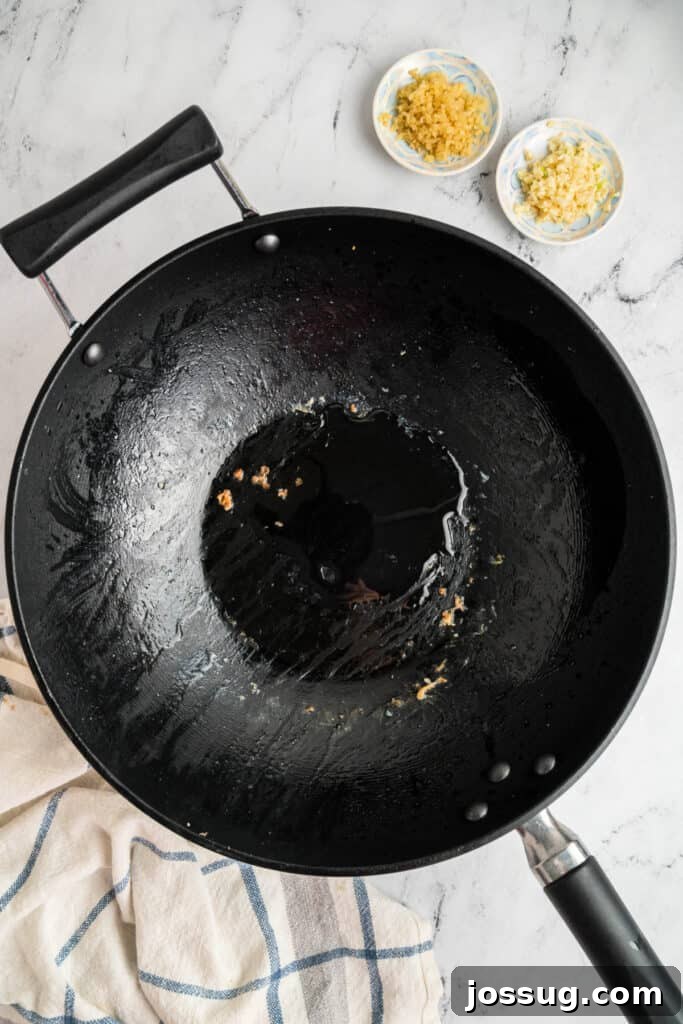 Empty wok with oil and bits of garlic and ginger left after cooking shrimp, indicating the next step for aromatics.