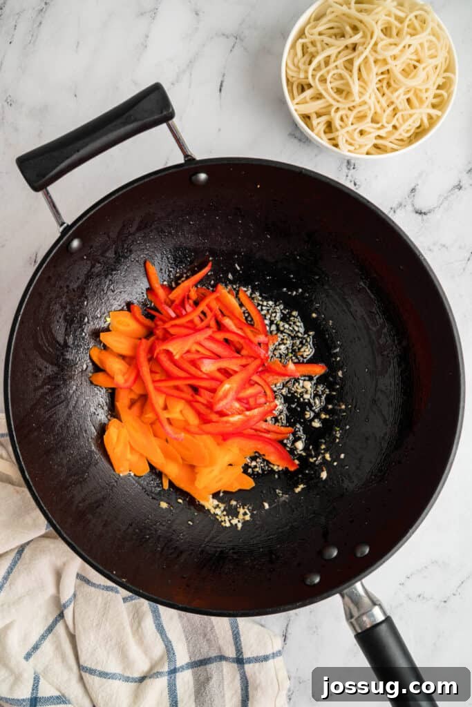 Carrots and red bell pepper strips added to the wok with garlic and ginger, demonstrating vegetable addition.