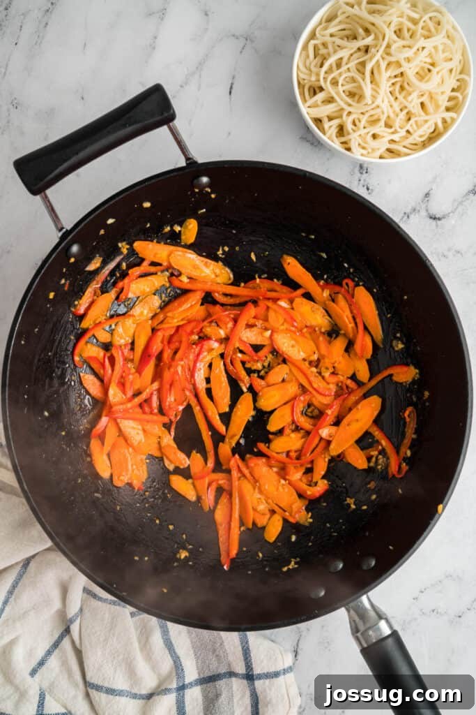 Sautéed carrots and red bell peppers cooking in the wok with garlic and ginger, showing the vegetables softening.