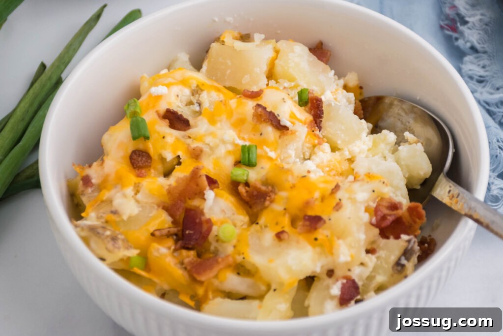 A serving of hot and bubbly Twice-Baked Potato Casserole in a white bowl, garnished with fresh green onions, showcasing its appetizing texture.