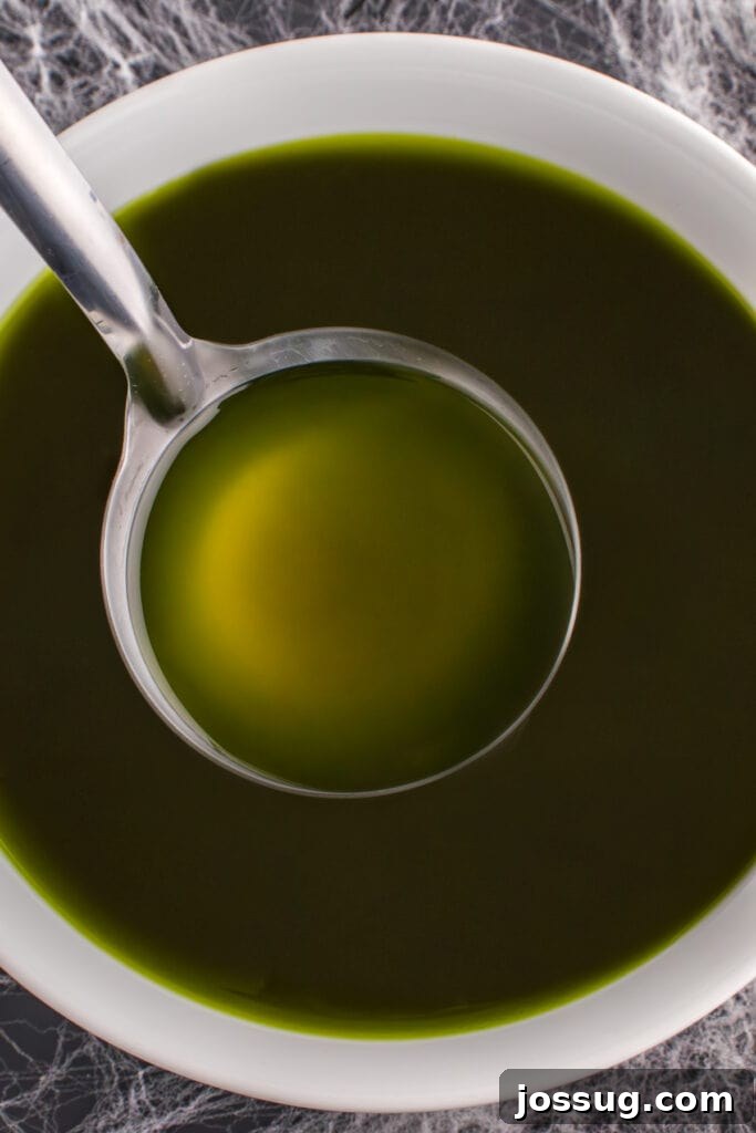 Biohazard Brew 13 A ladle gracefully dipping into a large bowl of dark green Toxic Waste Punch, positioned on a Halloween-themed table adorned with intricate cobweb decorations.