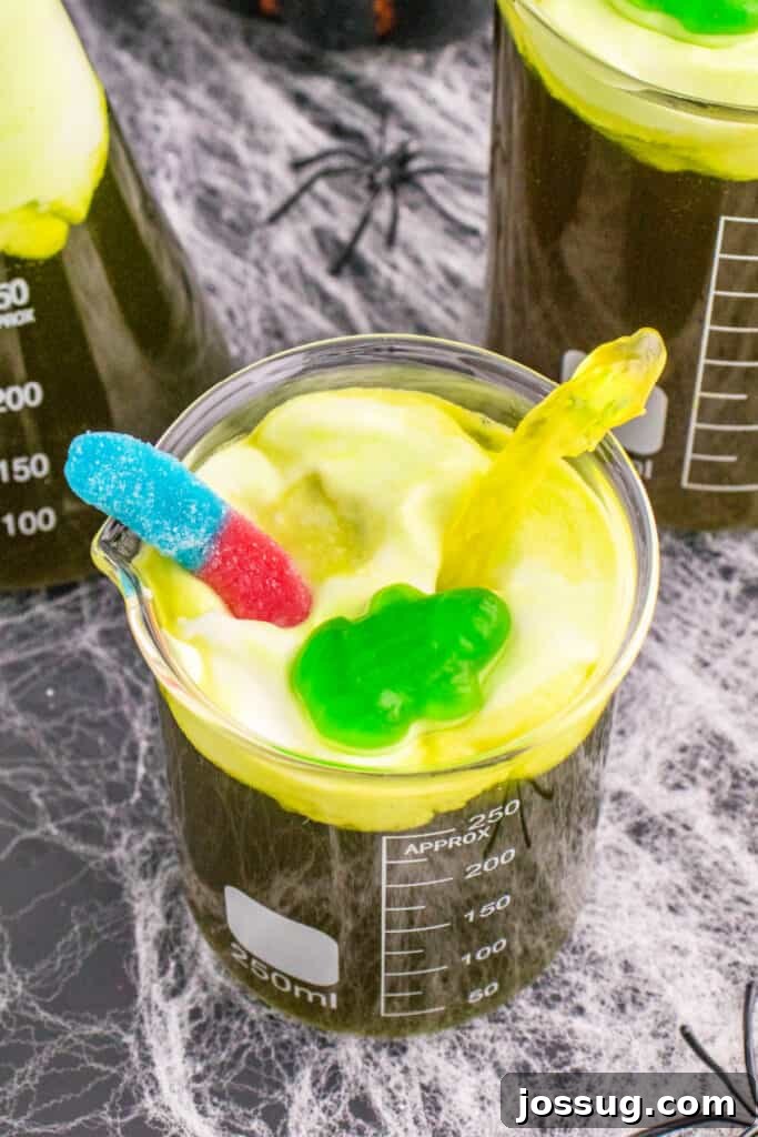 Biohazard Brew 17 A single beaker of Toxic Waste Punch, prominently featuring gummy frog and gummy worm toppings, perfectly showcasing the foamy toxic waste effect and enticing Halloween charm.