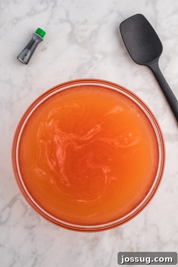 Biohazard Brew 6 Large glass bowl filled with orange punch mixture and a black spatula on the side with green food coloring bottle nearby, showing the initial mix.