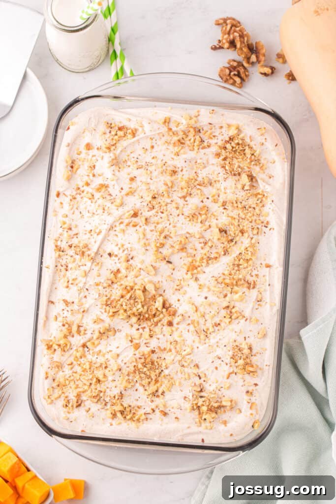 Spiced Golden Butternut Cake 12 The finished butternut squash cake, elegantly frosted with smooth cream cheese and garnished with a sprinkle of chopped walnuts, sits invitingly in a glass baking dish.