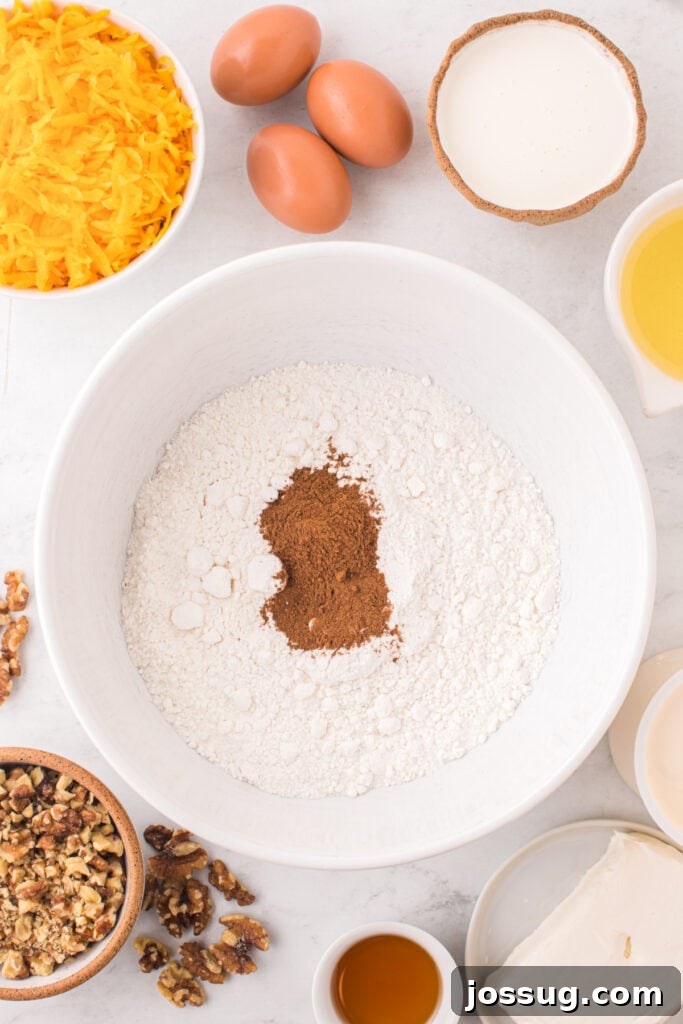 Spiced Golden Butternut Cake 4 A mixing bowl holds white cake mix and pumpkin pie spice, surrounded by essential ingredients: eggs, vibrant grated squash, rich cream, cooking oil, crunchy walnuts, and creamy cream cheese.
