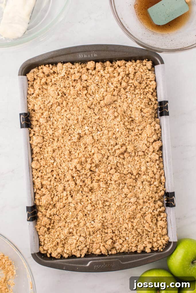 Baking pan filled with distinct layers of graham cracker crust, creamy cheesecake, spiced apples, and a generous crumb topping.