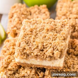 Square cut caramel apple cheesecake bar with crumb topping, styled on parchment paper.