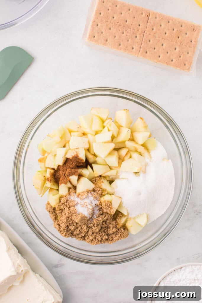 Bowl of chopped apples topped with granulated sugar, brown sugar, salt, and pumpkin pie spice, ready to be mixed for the filling.