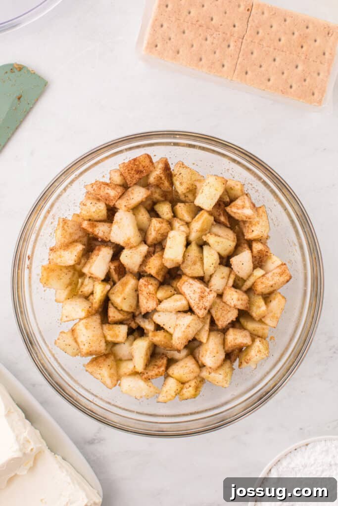 Mixed apple filling in a glass bowl, coated evenly with sugar and spices, ready for layering.